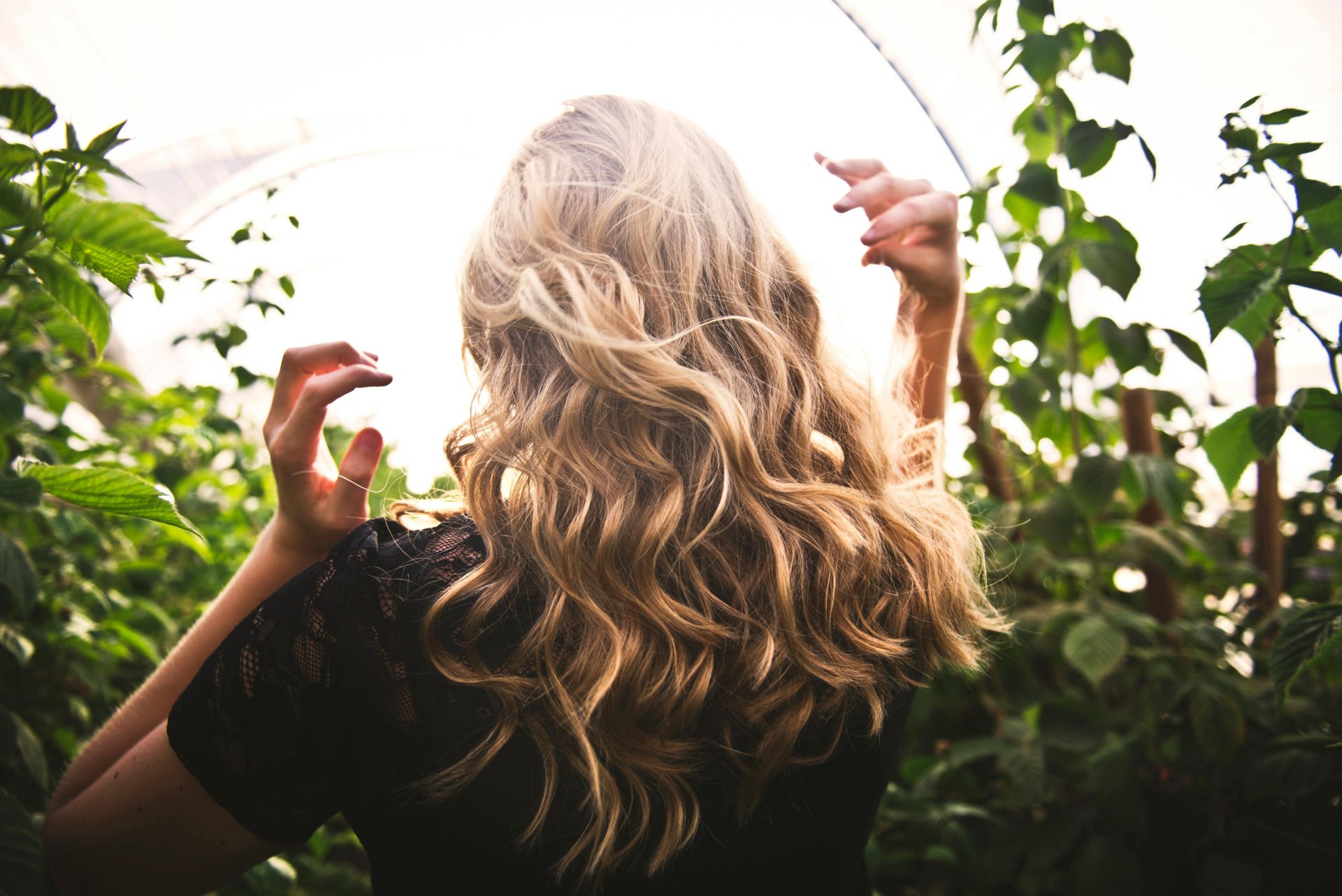 A woman with long blond curly hair, amongst leafy greenery